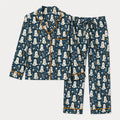 A two-piece pajama set featuring a long-sleeve button-front top and matching pants in a dark teal blue color, decorated with a repeating white ghost pattern and trimmed with orange piping.