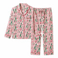 A two-piece pajama set featuring a long-sleeve button-front top and matching pants, both in a pink gingerbread print with green trees and red trim, shown on a plain white background.
