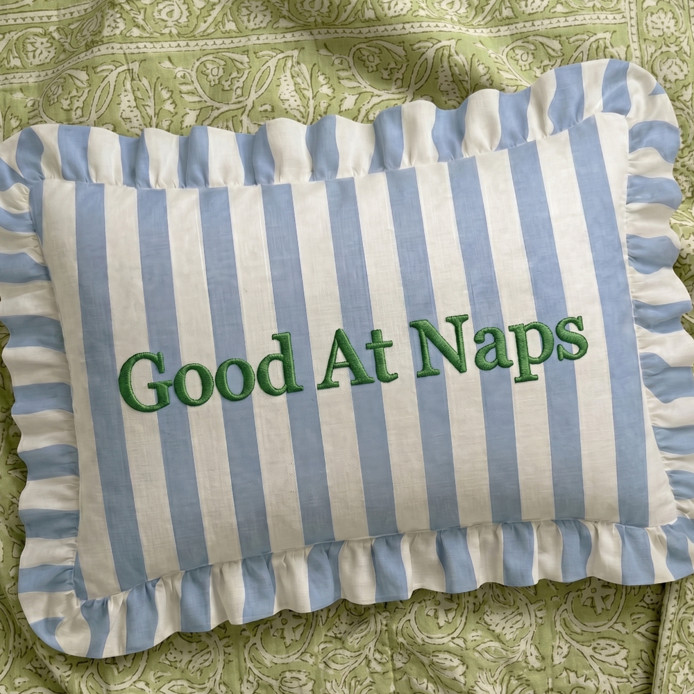 Striped pillow with 'Good At Naps' text on a green patterned background