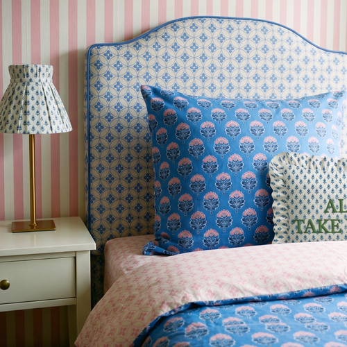 Bedroom with patterned headboard, pillows, and lamp against striped wall.
