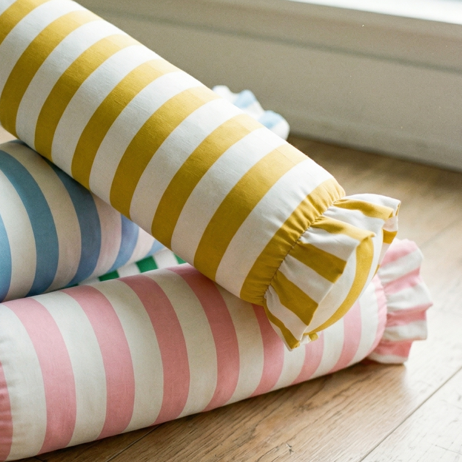 Striped cylindrical pillows in yellow, blue, and pink on a wooden floor.