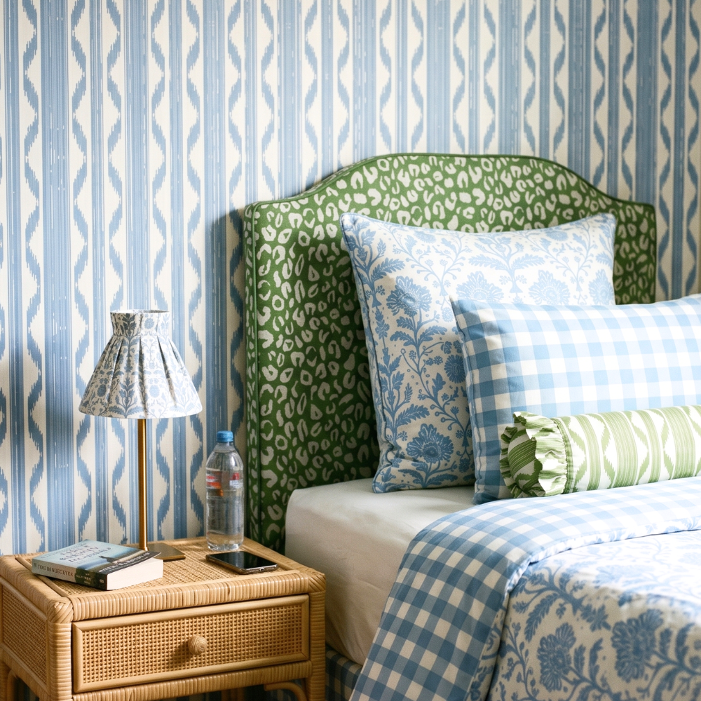 Bedroom with green headboard, blue and white bedding, and patterned wallpaper.