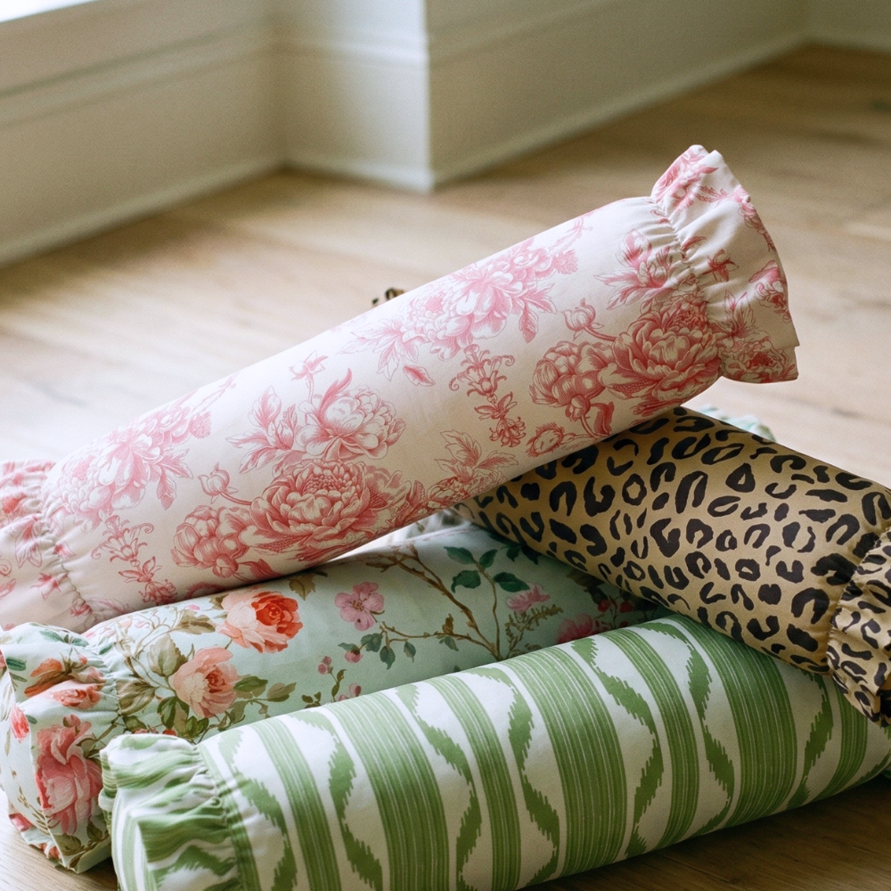 Stack of rolled-up fabric rolls with floral, leopard print, and striped patterns on a wooden floor.